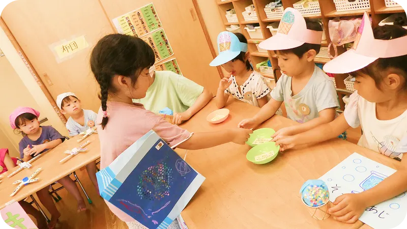 川辺で水遊びをしながら、バケツや砂遊び用のおもちゃで楽しむ子どもたちの様子