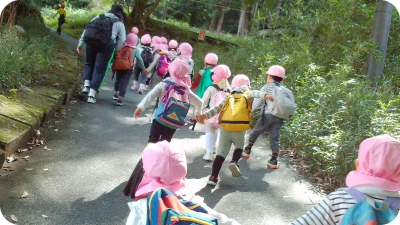 帽子とリュックを身につけて園外を列になって歩く園児たちの遠足の様子