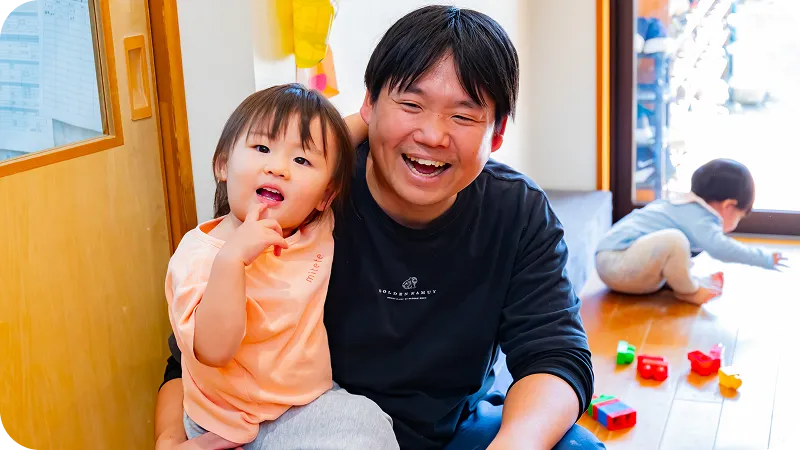 保育士と乳児が室内で楽しく遊んでいる様子