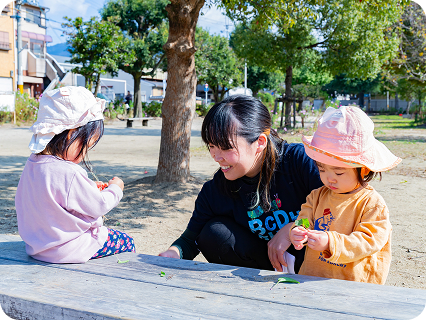園児がベンチに座りながら葉っぱで遊んでいる様子